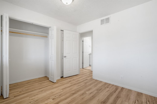 unfurnished bedroom with a textured ceiling, visible vents, baseboards, a closet, and light wood-type flooring