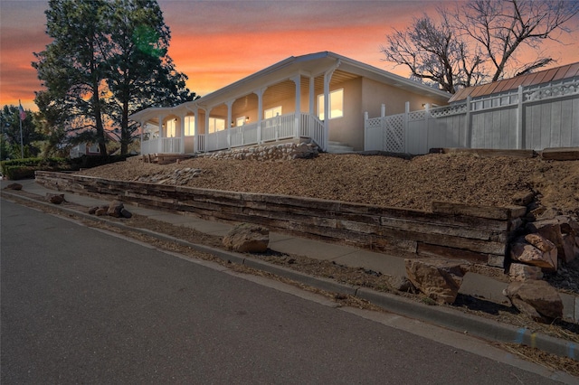 view of front of home featuring a porch, fence, and stucco siding