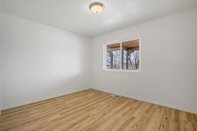 unfurnished room featuring a textured ceiling, light wood finished floors, visible vents, and baseboards