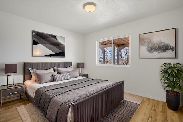 bedroom featuring a textured ceiling, baseboards, and wood finished floors