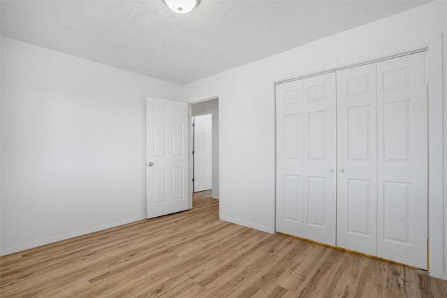 unfurnished bedroom featuring a textured ceiling, a closet, light wood-type flooring, and baseboards