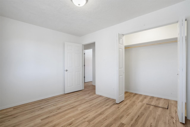 unfurnished bedroom featuring light wood finished floors, a textured ceiling, baseboards, and a closet