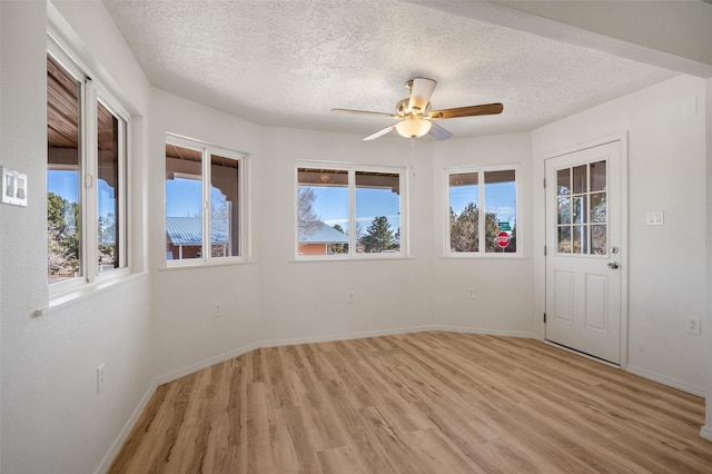 empty room with light wood-style flooring, baseboards, ceiling fan, and a textured ceiling