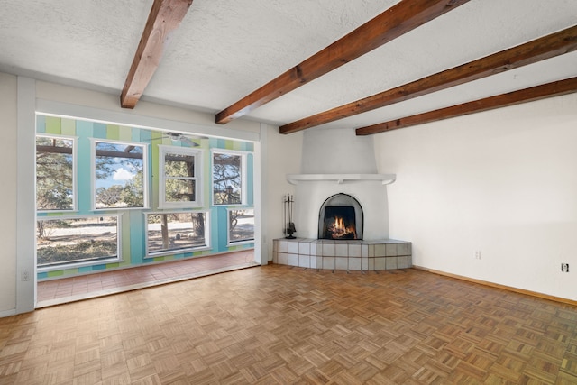 unfurnished living room featuring a textured ceiling, beamed ceiling, a tiled fireplace, and baseboards