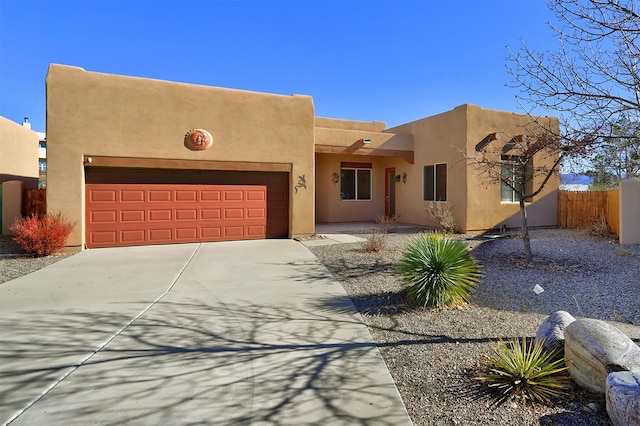 adobe home with a garage, driveway, fence, and stucco siding