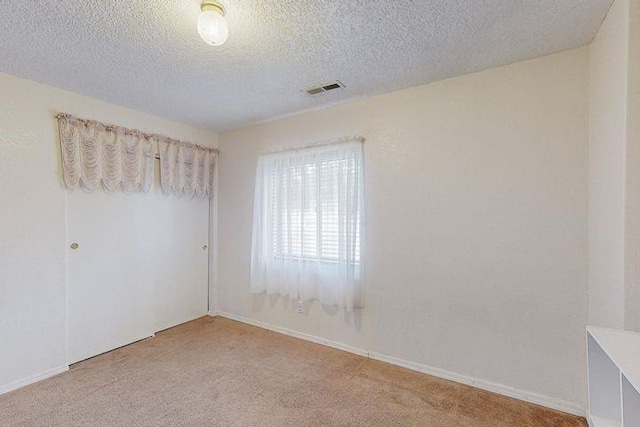 spare room featuring light carpet, a textured ceiling, visible vents, and baseboards