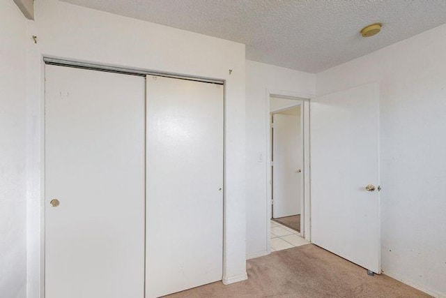 unfurnished bedroom with a closet, light colored carpet, and a textured ceiling