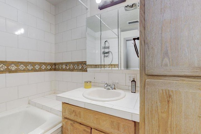 full bath featuring backsplash, tiled tub, vanity, and visible vents