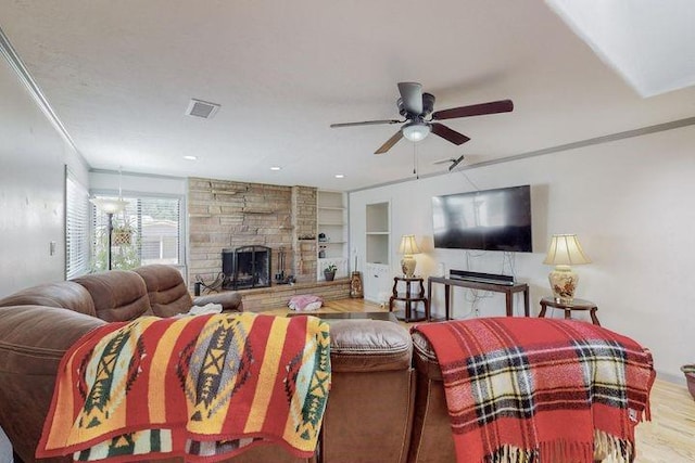 living area featuring built in features, a fireplace, ornamental molding, ceiling fan, and light wood-type flooring