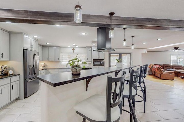 kitchen with island exhaust hood, dark countertops, hanging light fixtures, stainless steel fridge, and a kitchen breakfast bar