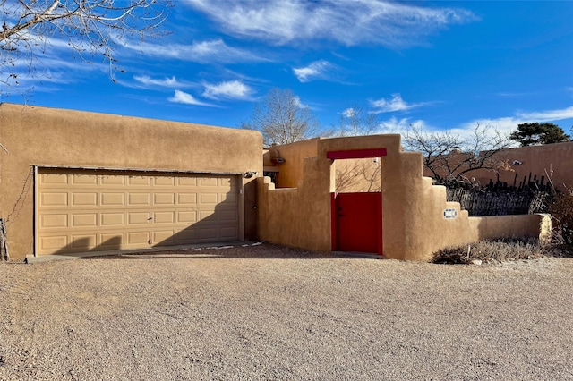 view of front of home with gravel driveway, an attached garage, fence, and stucco siding