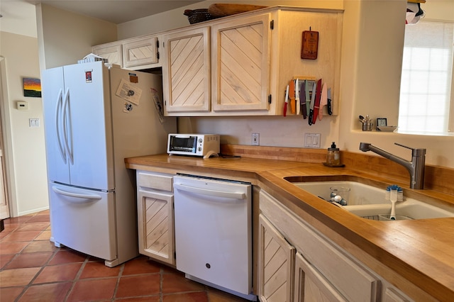 kitchen with dark tile patterned flooring, white appliances, a sink, and a toaster