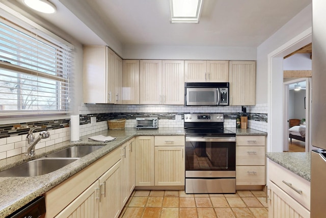 kitchen with appliances with stainless steel finishes, a sink, light stone countertops, and tasteful backsplash