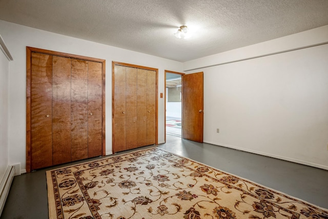 unfurnished bedroom featuring a textured ceiling, a baseboard radiator, concrete floors, and two closets