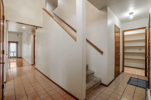 stairway with tile patterned flooring, a textured ceiling, baseboards, and a baseboard radiator