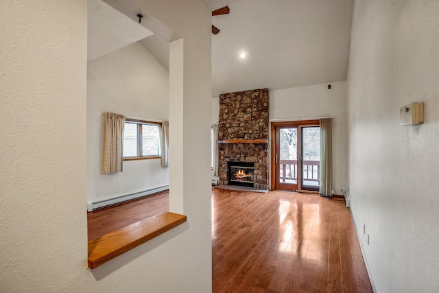 unfurnished living room featuring high vaulted ceiling, baseboard heating, wood finished floors, and a wealth of natural light