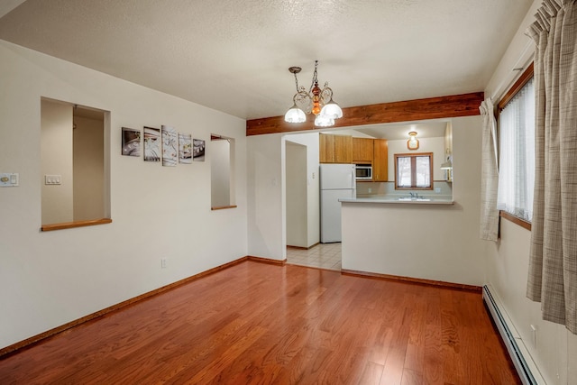 interior space featuring baseboards, light wood-style flooring, a textured ceiling, a baseboard heating unit, and a notable chandelier