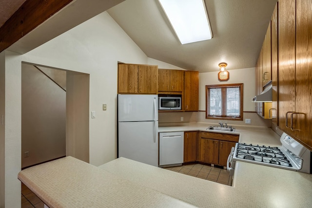 kitchen featuring light countertops, brown cabinetry, vaulted ceiling, a sink, and white appliances