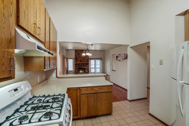 kitchen featuring under cabinet range hood, white appliances, light countertops, hanging light fixtures, and brown cabinetry