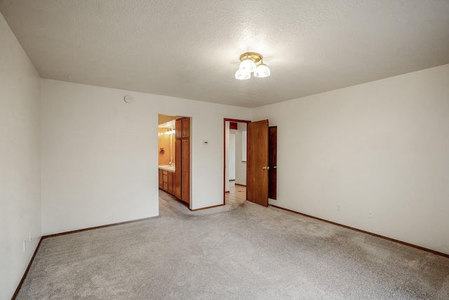 spare room featuring light carpet, a textured ceiling, and baseboards