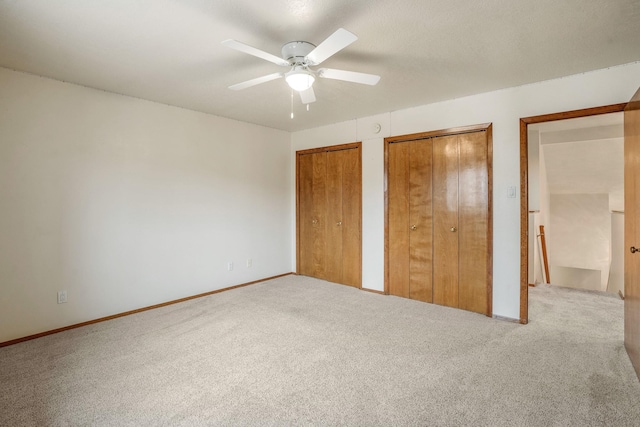 unfurnished bedroom featuring carpet floors, a ceiling fan, baseboards, and two closets