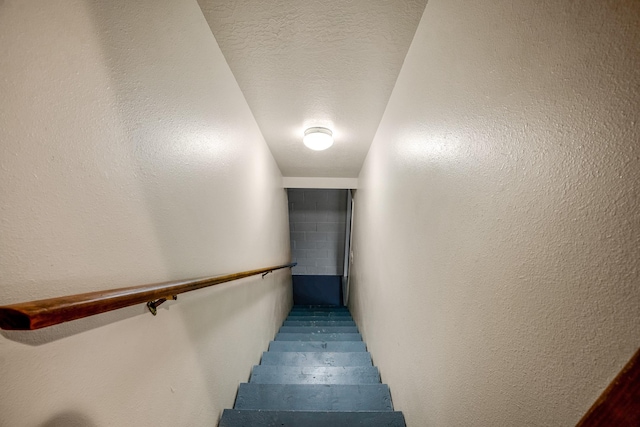 stairway with a textured ceiling and a textured wall