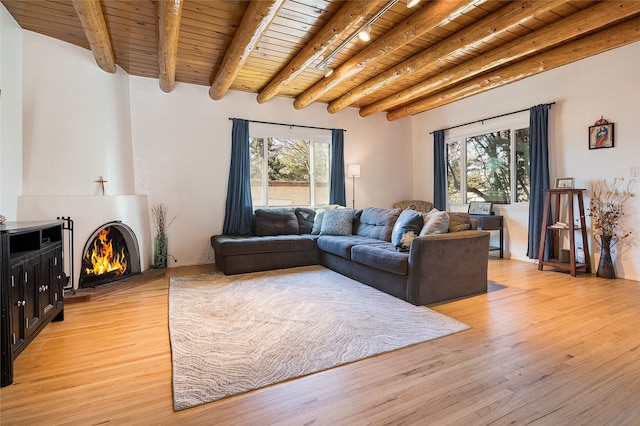 living area featuring a warm lit fireplace, plenty of natural light, wood ceiling, and light wood-style floors