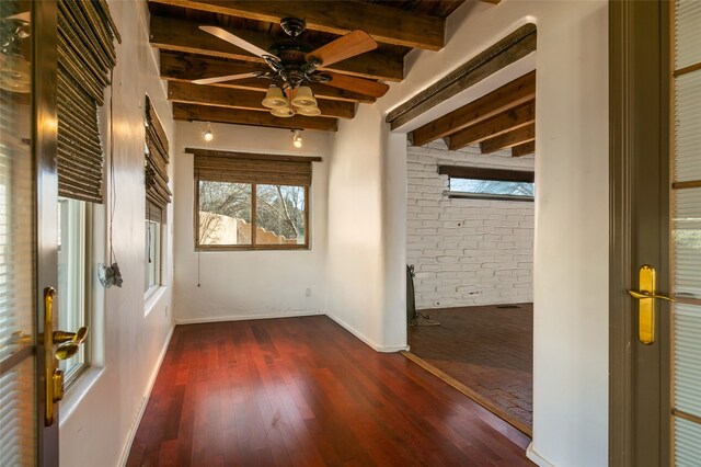 empty room with a ceiling fan, baseboards, dark wood finished floors, and beamed ceiling