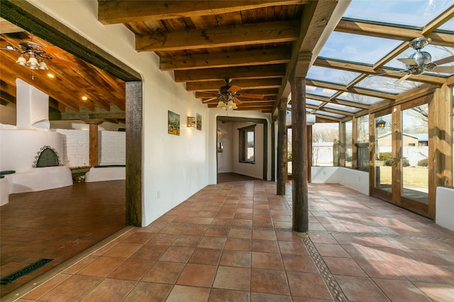 unfurnished sunroom featuring a ceiling fan, wood ceiling, and beamed ceiling