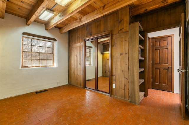 unfurnished bedroom with brick floor, wood ceiling, visible vents, and beam ceiling