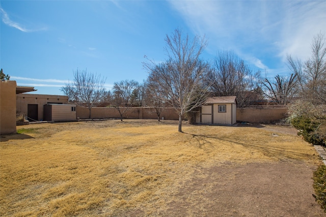 view of yard with a fenced backyard, a storage unit, and an outbuilding