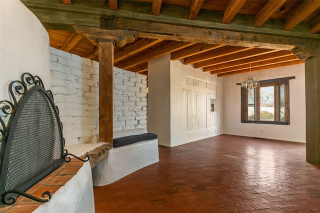 interior space with baseboards, brick floor, beam ceiling, and a notable chandelier