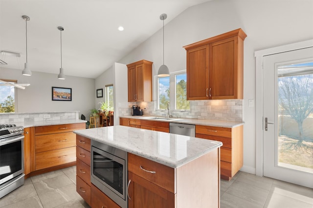 kitchen with a sink, vaulted ceiling, appliances with stainless steel finishes, a center island, and decorative light fixtures