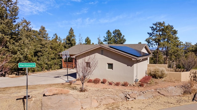 view of home's exterior with fence, solar panels, and stucco siding