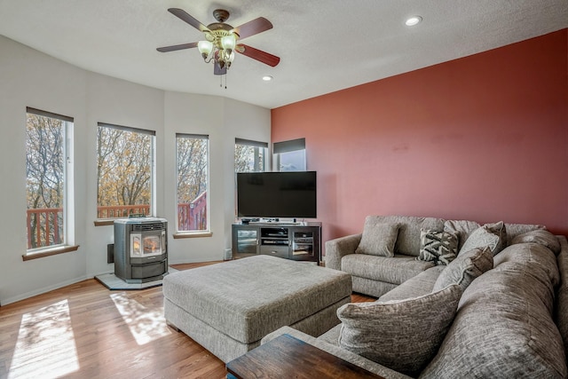 living area featuring baseboards, ceiling fan, a wood stove, light wood-type flooring, and recessed lighting