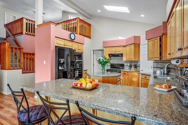 kitchen featuring a breakfast bar, a sink, a peninsula, under cabinet range hood, and black appliances