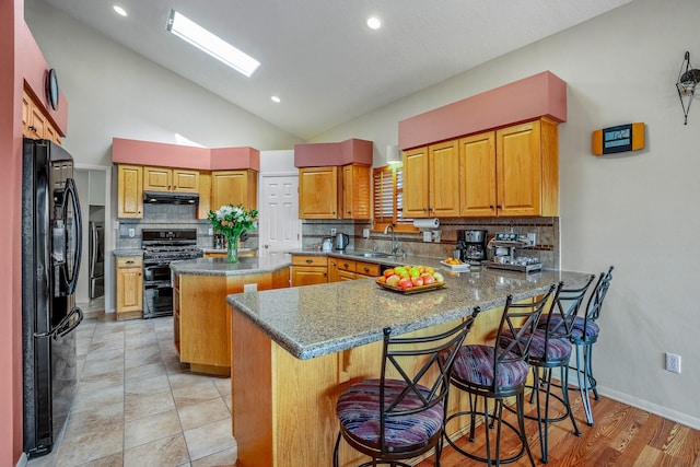 kitchen with a center island, a peninsula, black appliances, a kitchen bar, and a sink