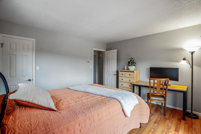 bedroom featuring light wood-type flooring, baseboards, and a textured ceiling