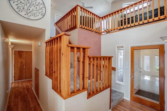 stairs with a high ceiling, wood finished floors, and baseboards