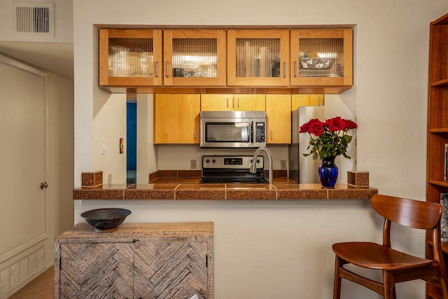 kitchen with glass insert cabinets, visible vents, stainless steel appliances, and a breakfast bar area