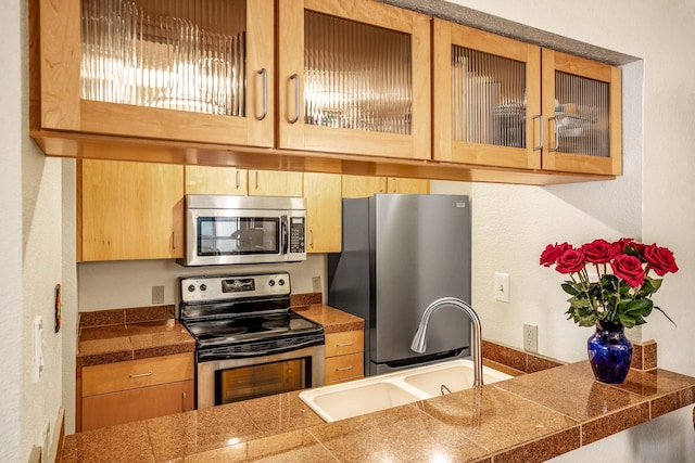 kitchen with appliances with stainless steel finishes, tile counters, glass insert cabinets, and a sink