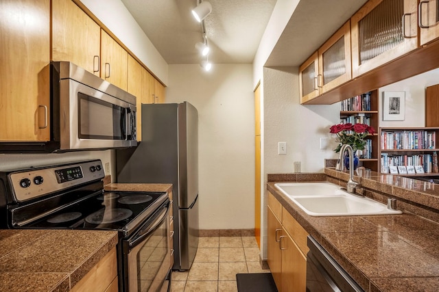 kitchen featuring tile countertops, light tile patterned floors, stainless steel appliances, glass insert cabinets, and a sink