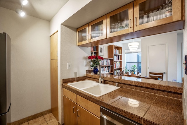 kitchen with light tile patterned floors, tile countertops, appliances with stainless steel finishes, glass insert cabinets, and a sink