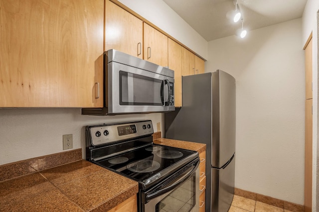 kitchen featuring baseboards, tile countertops, appliances with stainless steel finishes, rail lighting, and light brown cabinetry