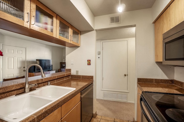 kitchen with appliances with stainless steel finishes, glass insert cabinets, a sink, and visible vents