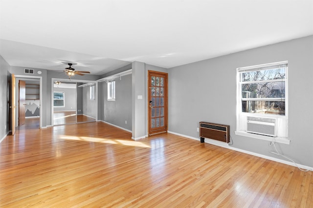 unfurnished living room with light wood-style floors, baseboards, plenty of natural light, and heating unit