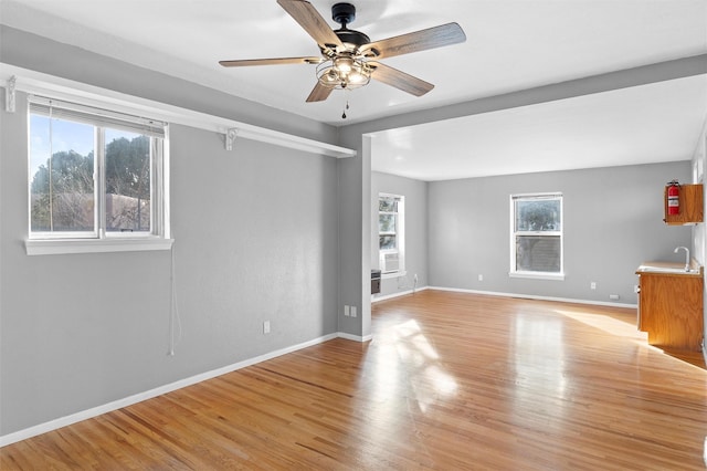 empty room featuring a ceiling fan, a sink, light wood-style flooring, and baseboards