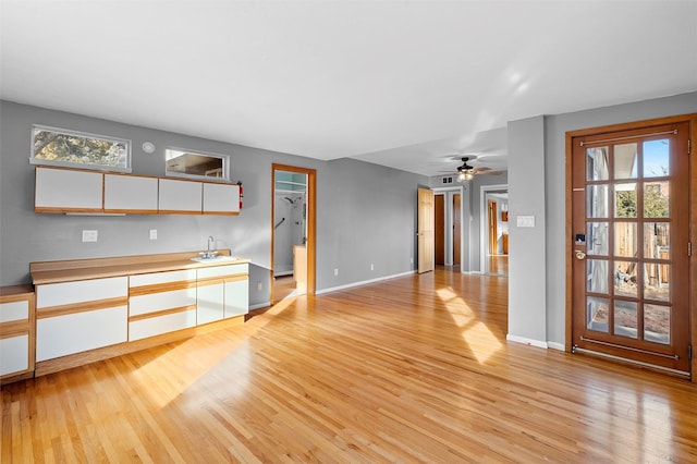 unfurnished living room featuring a wealth of natural light, a sink, light wood-style flooring, and baseboards