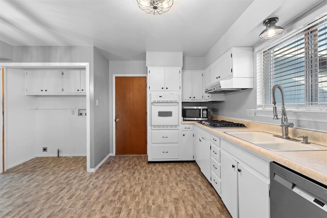 kitchen with stainless steel appliances, a sink, white cabinetry, light countertops, and light wood finished floors