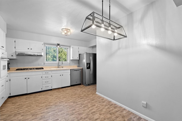 kitchen with decorative light fixtures, light countertops, appliances with stainless steel finishes, white cabinets, and a sink